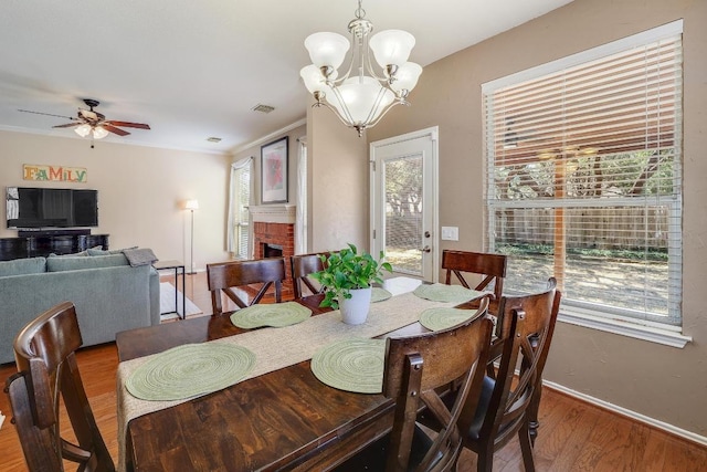 dining room with a healthy amount of sunlight, a brick fireplace, visible vents, and wood finished floors