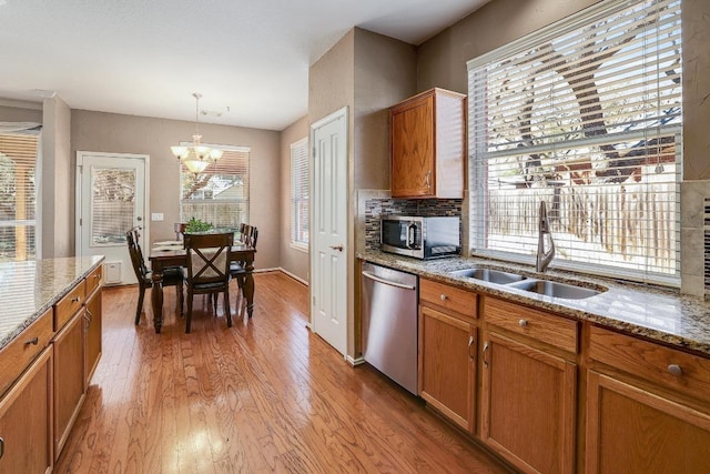 kitchen with tasteful backsplash, light wood-style flooring, appliances with stainless steel finishes, brown cabinets, and a sink