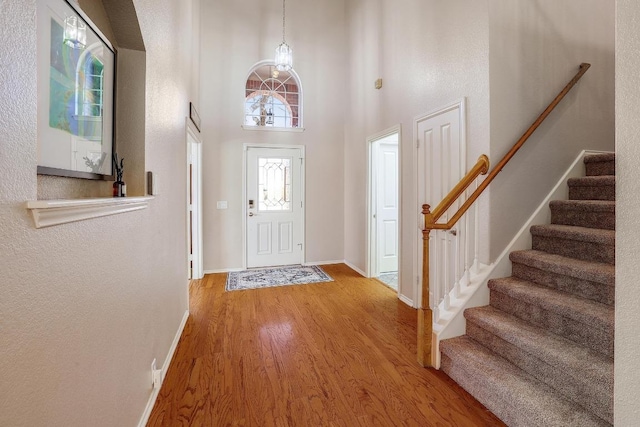 foyer entrance featuring baseboards, stairway, wood finished floors, an inviting chandelier, and a high ceiling