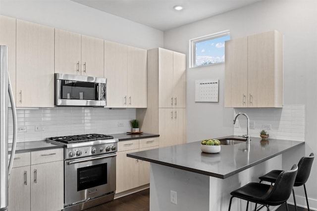 kitchen with a peninsula, dark countertops, appliances with stainless steel finishes, and a sink