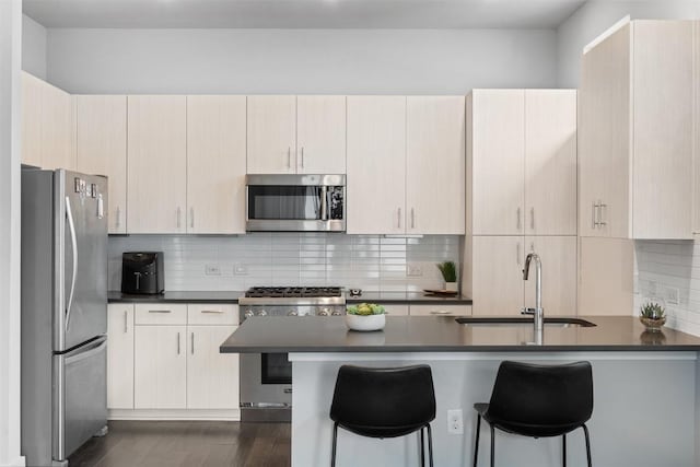 kitchen with dark countertops, appliances with stainless steel finishes, a peninsula, a sink, and backsplash