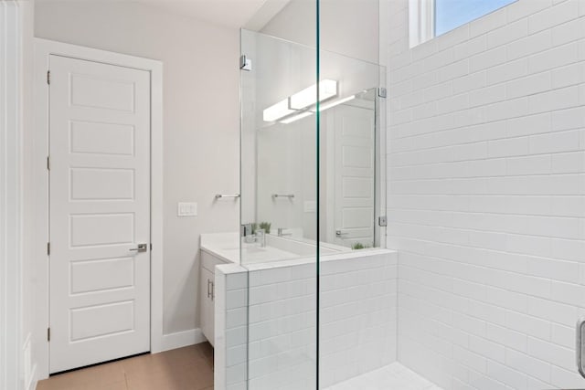 full bath featuring a stall shower, vanity, baseboards, and wood finished floors