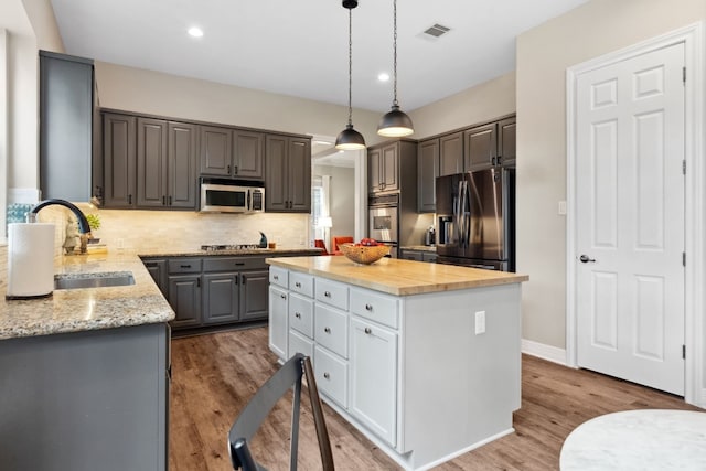 kitchen featuring stainless steel appliances, a sink, a kitchen island, visible vents, and tasteful backsplash