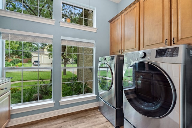 clothes washing area featuring baseboards, washer and clothes dryer, cabinet space, and light wood-style floors