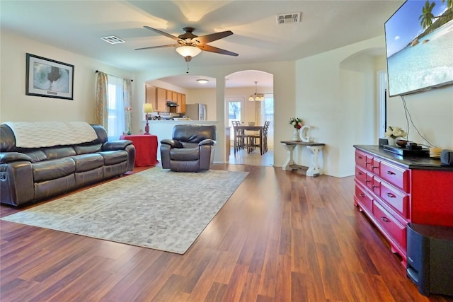 living room featuring arched walkways, dark wood-style flooring, plenty of natural light, and visible vents