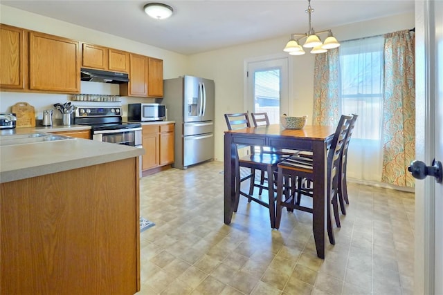 kitchen with under cabinet range hood, stainless steel appliances, a sink, light countertops, and decorative light fixtures