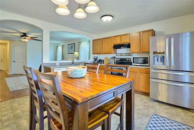 kitchen with arched walkways, under cabinet range hood, a ceiling fan, light countertops, and appliances with stainless steel finishes