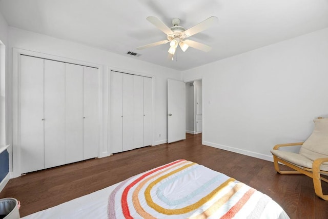 bedroom with baseboards, visible vents, two closets, and wood finished floors