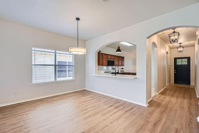 interior space with arched walkways, light wood-style floors, a sink, a chandelier, and baseboards