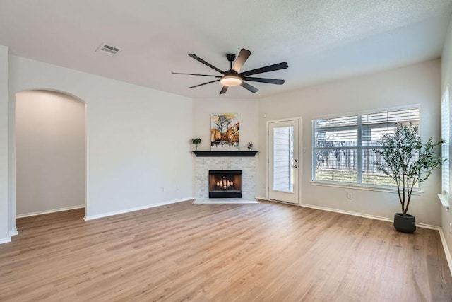 unfurnished living room with ceiling fan, a warm lit fireplace, visible vents, baseboards, and light wood-type flooring