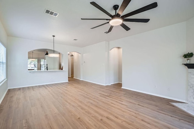 unfurnished living room with arched walkways, visible vents, a ceiling fan, wood finished floors, and baseboards