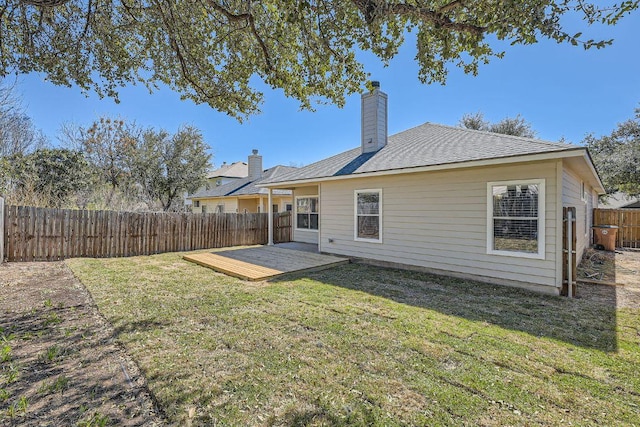 back of property with a deck, a fenced backyard, a yard, and a chimney