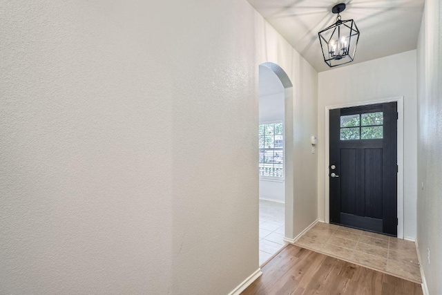 foyer entrance featuring light wood-style floors, arched walkways, baseboards, and an inviting chandelier