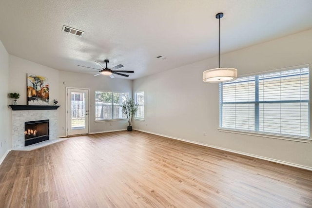 unfurnished living room with a fireplace with flush hearth, a textured ceiling, wood finished floors, and visible vents