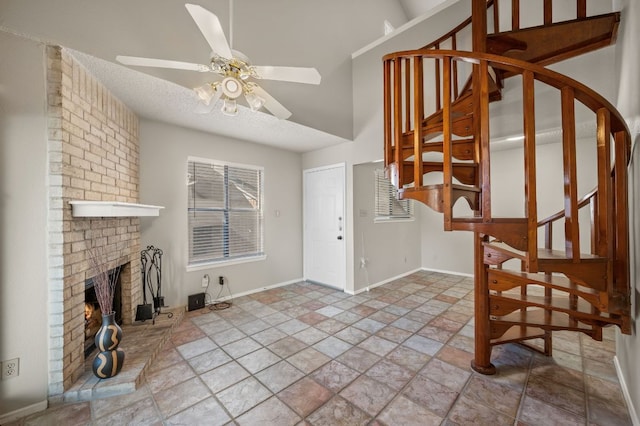 foyer entrance with baseboards, a ceiling fan, stairs, a brick fireplace, and a wealth of natural light