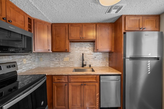 kitchen featuring visible vents, appliances with stainless steel finishes, brown cabinetry, and a sink