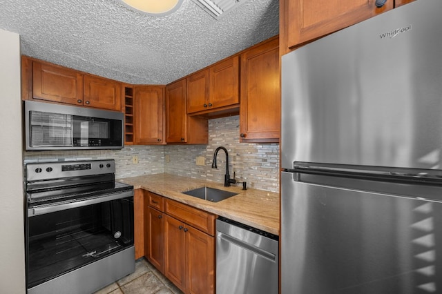 kitchen featuring brown cabinets, backsplash, appliances with stainless steel finishes, a sink, and a textured ceiling