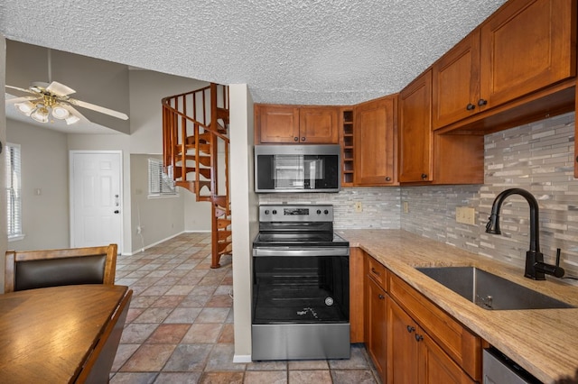 kitchen featuring stainless steel appliances, a sink, a ceiling fan, brown cabinets, and decorative backsplash