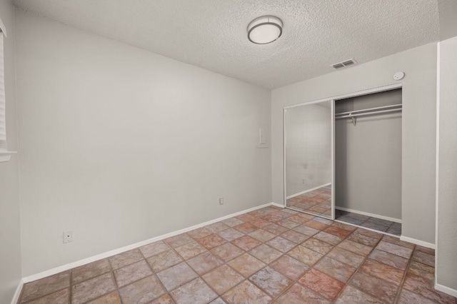 unfurnished bedroom with a textured ceiling, visible vents, baseboards, a closet, and stone finish floor