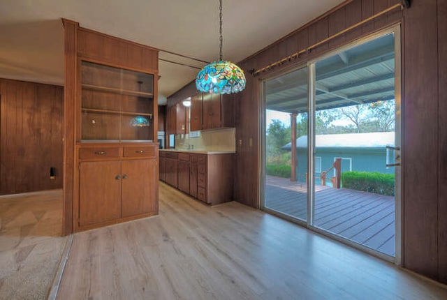 kitchen with decorative light fixtures, light wood-type flooring, brown cabinets, and wooden walls