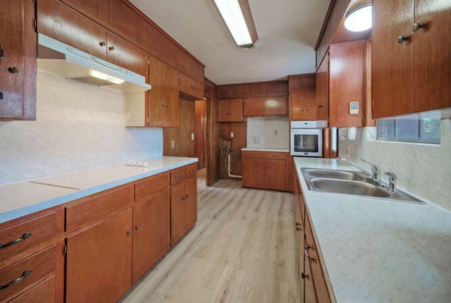 kitchen featuring brown cabinets, white oven, light countertops, light wood-style floors, and a sink