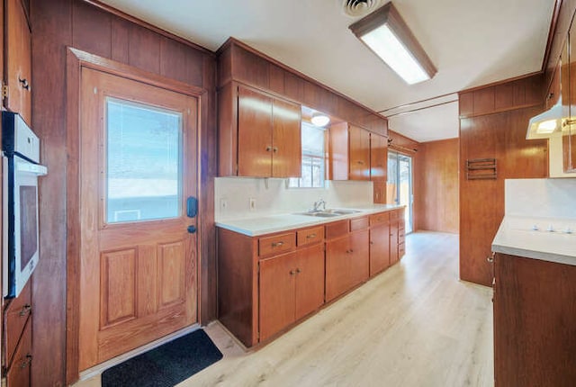 kitchen featuring brown cabinetry, light wood-style flooring, white oven, light countertops, and a sink