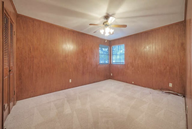 unfurnished room featuring light carpet, ceiling fan, and wooden walls