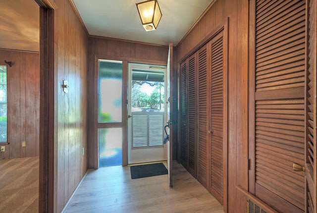 doorway with light wood-type flooring and wood walls