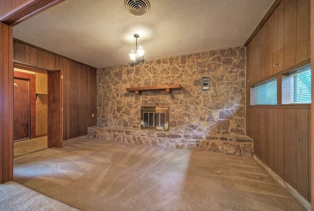 unfurnished living room with carpet, wooden walls, visible vents, and a stone fireplace