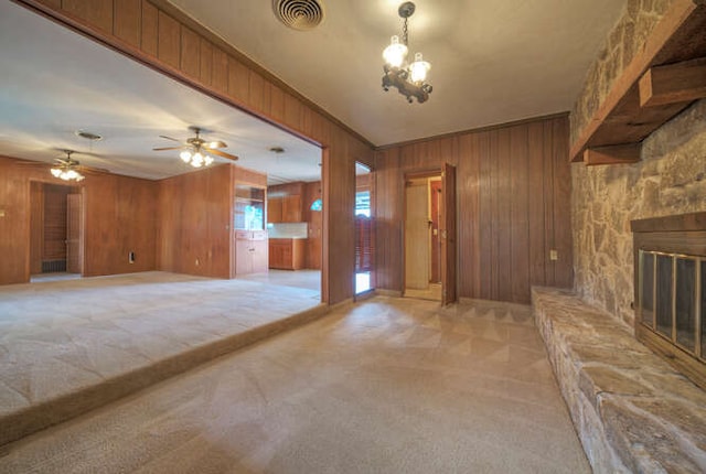 unfurnished living room with ceiling fan, wooden walls, light colored carpet, a fireplace, and visible vents