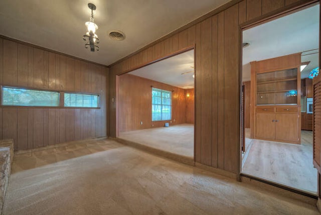 empty room featuring carpet, visible vents, and wooden walls