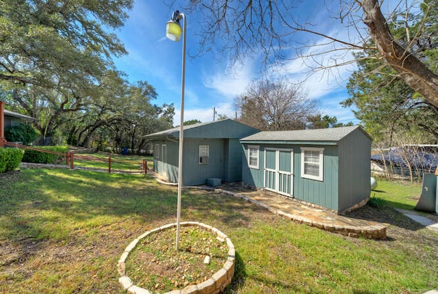 rear view of property with fence, a lawn, and an outbuilding