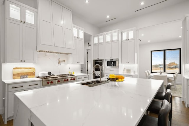 kitchen featuring stainless steel appliances, recessed lighting, white cabinets, a sink, and a large island with sink