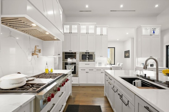 kitchen featuring custom exhaust hood, stainless steel appliances, white cabinets, a sink, and wood finished floors