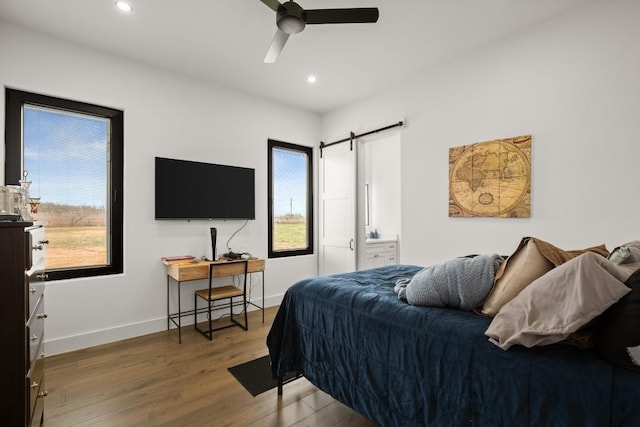 bedroom featuring recessed lighting, wood finished floors, baseboards, and a barn door