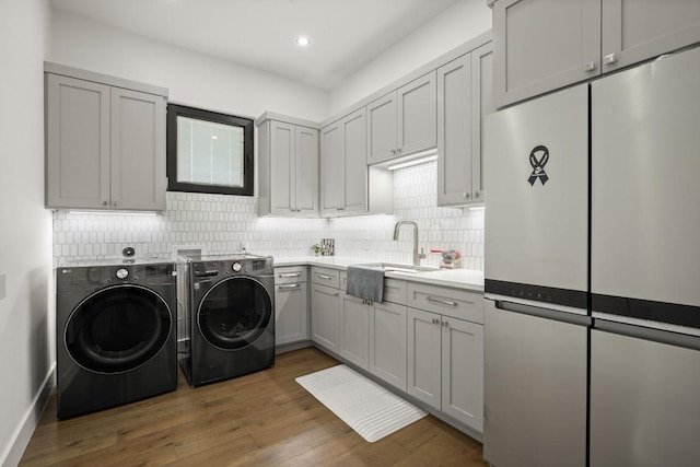 clothes washing area featuring recessed lighting, wood finished floors, a sink, washer and dryer, and cabinet space