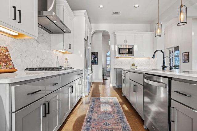 kitchen with visible vents, arched walkways, wall chimney exhaust hood, stainless steel appliances, and gray cabinetry