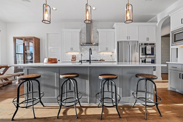 kitchen featuring arched walkways, stainless steel appliances, light countertops, decorative backsplash, and a large island with sink