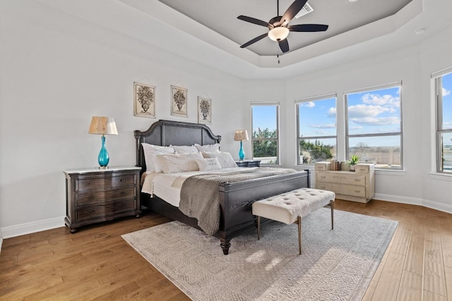 bedroom with a raised ceiling, visible vents, wood-type flooring, ceiling fan, and baseboards