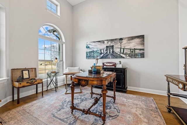 office space featuring baseboards, a high ceiling, wood finished floors, and a healthy amount of sunlight