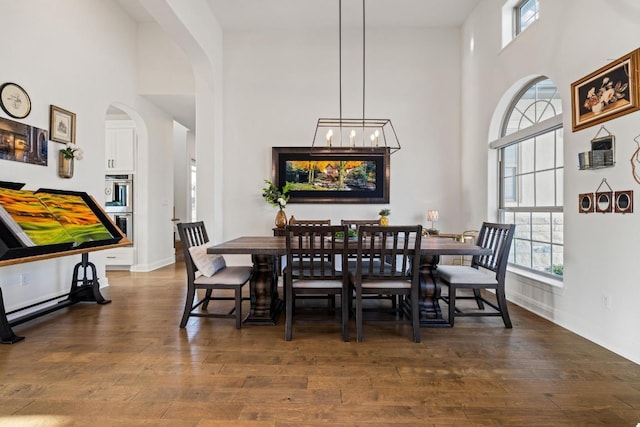 dining space with arched walkways, baseboards, a high ceiling, and hardwood / wood-style flooring