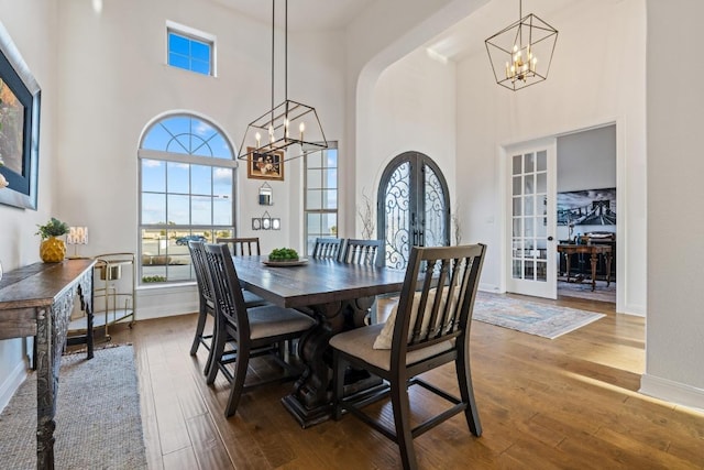 dining area featuring arched walkways, french doors, a notable chandelier, a healthy amount of sunlight, and hardwood / wood-style flooring