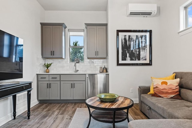 kitchen with dishwashing machine, a wall unit AC, gray cabinetry, and wood finished floors