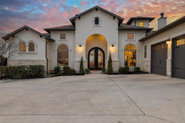 view of front of home featuring french doors, stucco siding, concrete driveway, a garage, and stone siding