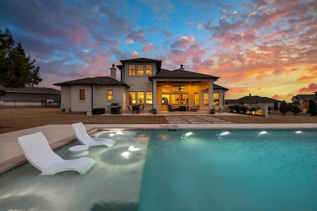 pool at dusk featuring an outdoor pool, a patio area, fence, and grilling area