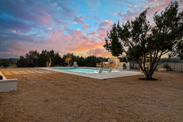 pool at dusk with a yard, a patio area, fence, and an outdoor pool