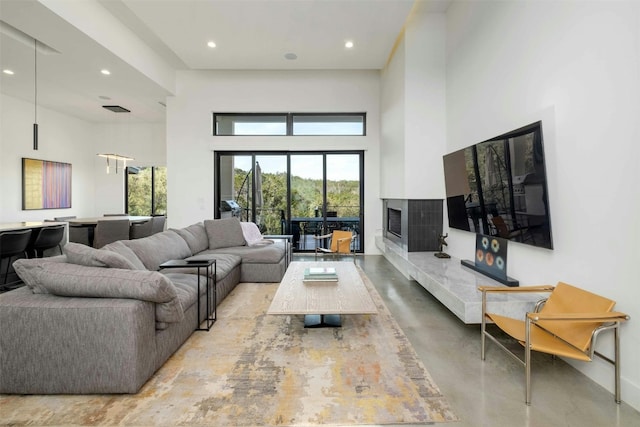 living room featuring a towering ceiling, a fireplace, concrete flooring, and recessed lighting