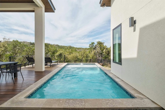 view of swimming pool with a wooded view and a fenced in pool