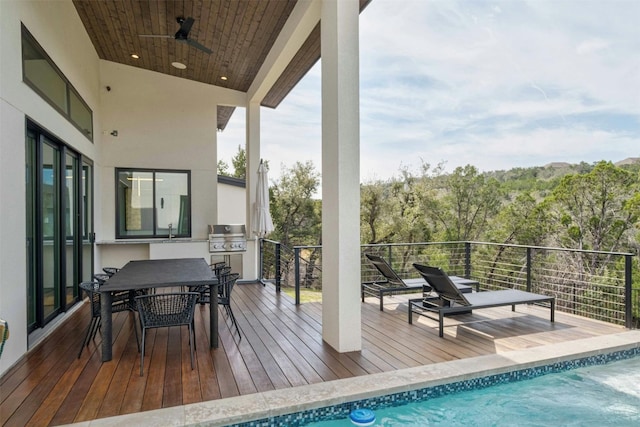 wooden deck with outdoor dining space, a grill, ceiling fan, a sink, and a wooded view