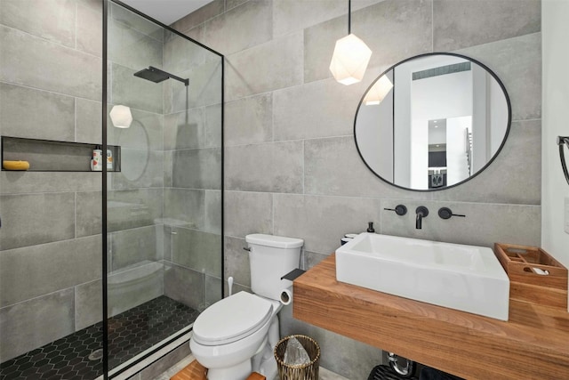 bathroom featuring a sink, a tile shower, toilet, and tile walls